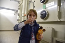 Kind steht vor den Filtern im Wasserwerk Lobberich und trinkt ein Glas Trinkwasser